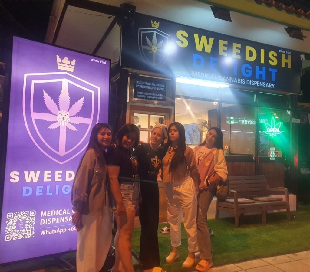 Sweedish Delight dispensary staff standing outside illuminated storefront at night with neon open sign.